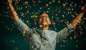 Person celebrating with multi-colored confetti. Topic: Green America’s Guide to Sustainable Gifts, Holidays, and Special Occasions.