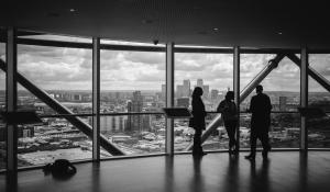 black and white photo of three people talking in front of a large panoramic window overlooking the city.