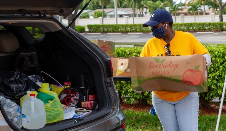 person putting a box of food into the trunk of a car
