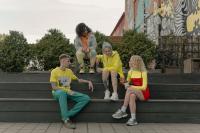 A brightly dressed group of young people sitting on large, concrete steps outside. They are talking. Gen Z finances.
