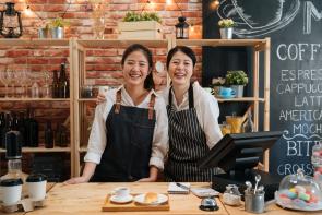mother and daughter wearing aprons and smiling. They are coffee shop owners ready to make coffee.