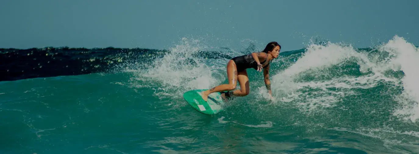 A filipina woman in a black one piece bathing suit surfing on turquoise blue waves.