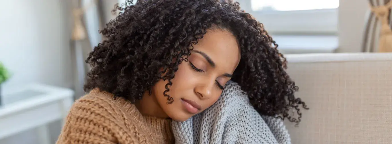 A Black woman relaxing and cuddling with a gray knitted blanket.