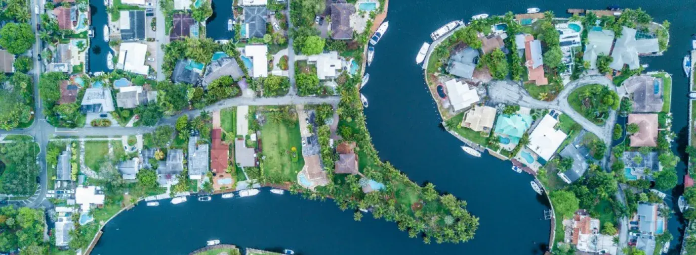 Drone image of a neighborhood in Fort Lauderdale, Florida. A winding river runs through the neighborhood. Homes have dock and boat access to the water.