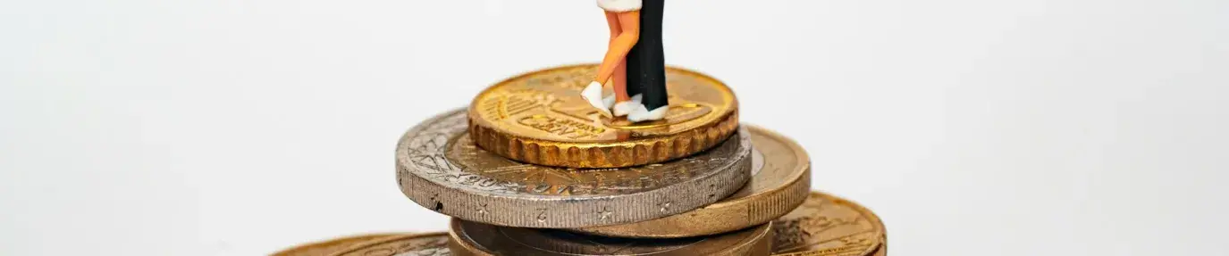 Two clay figures in a romantic embrace stand atop a pile of gold coins. Valentine's Day love money.