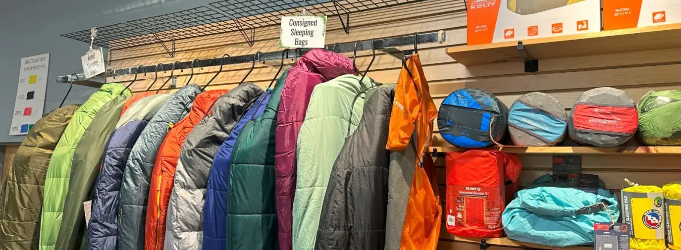 rows of gently used sleeping bags rest on hangers next to sleeping pads and camp pillows.