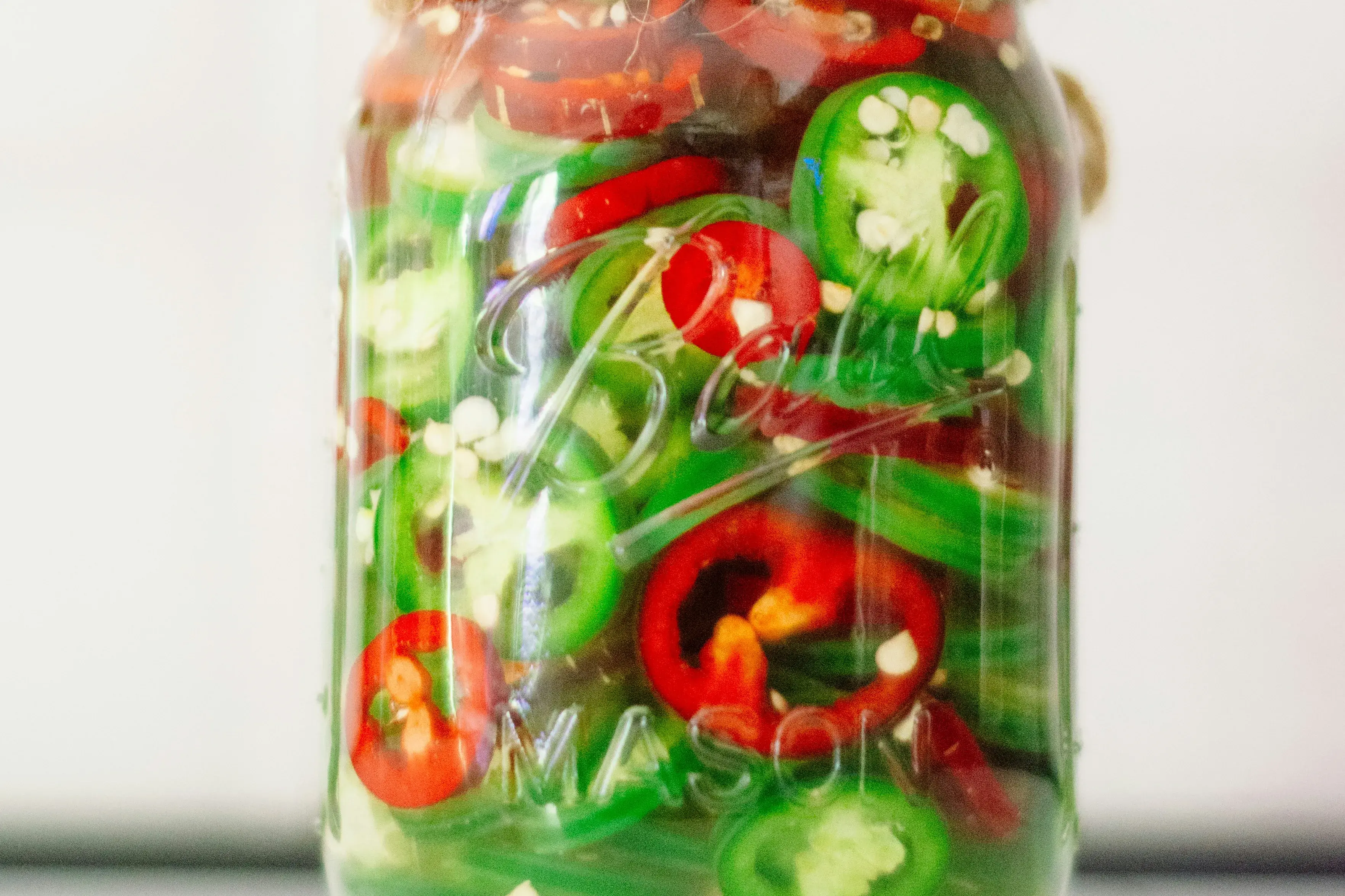 Beautiful slices of bright red and bright green sliced peppers in a canning jar. They are submerged in liquid. 